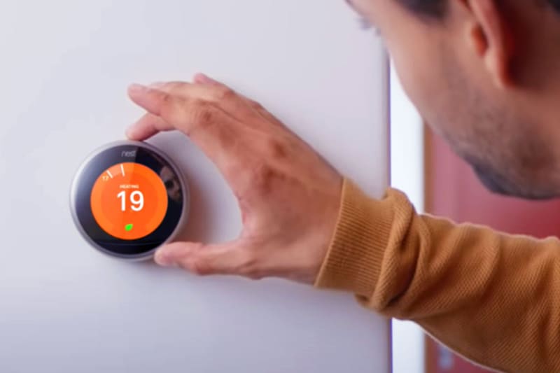 Hand adjusting a smart heating thermostat on the wall